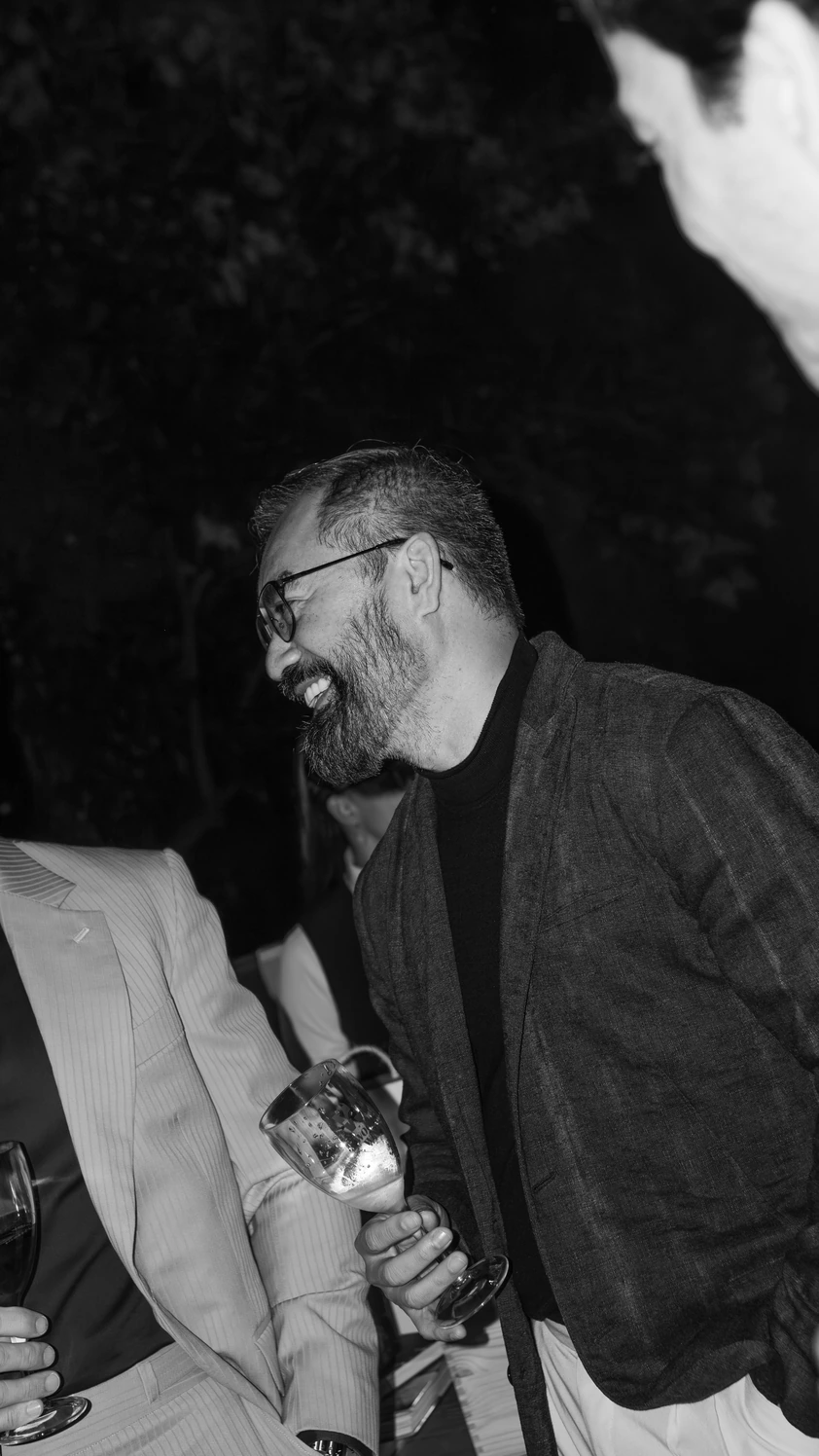 Convidado sorrindo com taça na mão durante evento, em preto e branco
